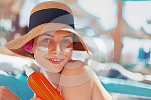 Young woman with sun cream on face holding sunscren bottle on the beach.