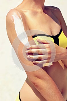 Young woman with sun cream on the shoulder relaxing on the beach