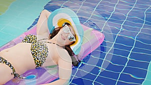 A young woman in sun glasses tans on an inflatable mattress, swims in the pool