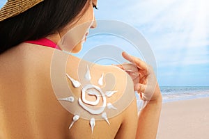 Young woman with sun protection cream on her back at beach