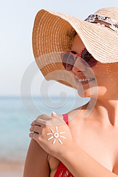 Young woman with sun shape on her hand made of sunscreen at the beach