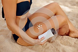 Young woman with sun shape on the legs holding sun cream bottle on the beach.Sunscreen Solar Cream.