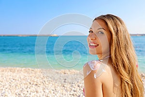 Young woman with sun shape on the shoulder. Beautiful happy cute woman applying suntan cream on her shoulder with beach background