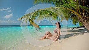 Young woman sunbathes in shade of palm tree near ocean water