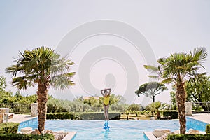 Young woman sunbathing while standing on the edge of the pool, putting her hands behind her head and looking to the side