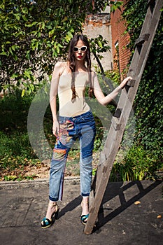 young woman with sunglasses and blue jeans and high heels in backyard summer fashion