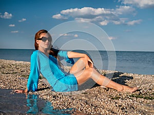 Young woman in sunglasses, blue tunika sits at the seaside and looks at the sea at sunny day Beautiful Smiling Woman Laughing On S