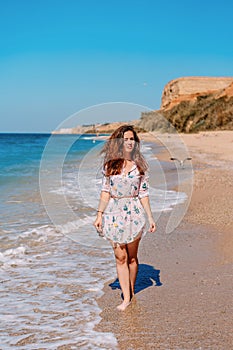Young woman in sunglasses and dress on the beach in front of the sea photo