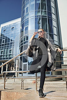 Young woman in sunglasses have walk outdoors near business building at sunny daytime