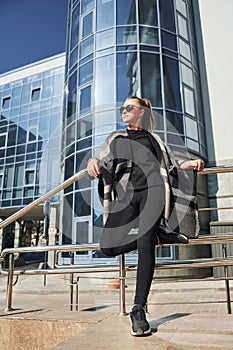 Young woman in sunglasses have walk outdoors near business building at sunny daytime