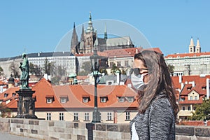 Young woman with sunglasses and medical face mask on the Charles Bridge in Prague, Czech Republic. Blurred old town and Prague