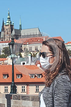 Young woman with sunglasses and medical face mask on the Charles Bridge in Prague, Czech Republic. Blurred old town and Prague