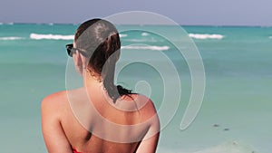 Young Woman in Sunglasses and Red Bikini Sitting and Looking at Ocean, Rear view