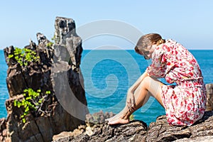 Young woman with sunglasses sitting on rocks near the sea.