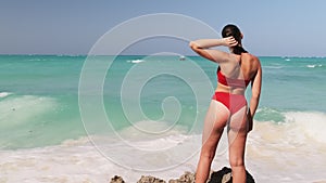 Young Woman in Sunglasses Standing in Red Bikini and Looks to Ocean, Rear View