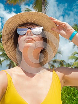 A young woman in sunglasses and a straw hat on a tropical island.