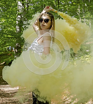 Young woman in sunglasses and summer clothes using smoke bomb