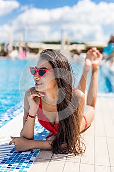 Young woman in sunglasses sunbathing near swimming pool