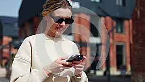 Young woman in sunglasses using mobile phone while taking walk in urban area