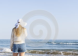 Young woman in sunhat standing on the beach,enjoying and looking at the ocean.Outdoor summer vacation lifestyle concept.Travel and
