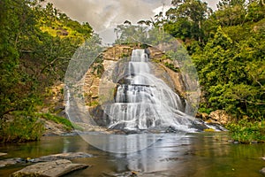 Young woman in a Sunny day in the Tropical waterfall falls from the mountain cliff to the jungle, serene landscape of Diyaluma fal