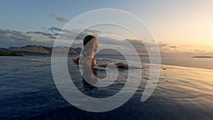 young woman at sunset in infinity pool on edge of abyss. girl looks into distance, concept of loneliness and happiness