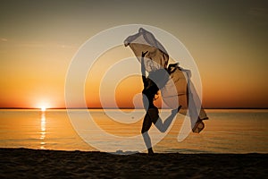 Young woman at sunset jumping on the seashore with background of the sky