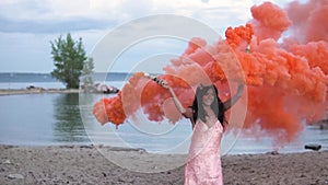 Young woman at sunset waving red smoke bombs