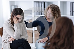 Young woman supporting sad patient at Women`s issues support group