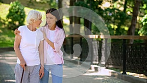 Young woman supporting sick aged lady walking stick, illness depression, rehab