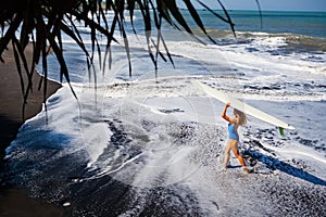 Young woman with surfboard walk on black sand beach