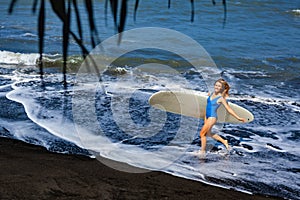 Young woman with surfboard walk on black sand beach