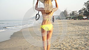 Young woman surfer walks with a surfboard along the sea sandy coast