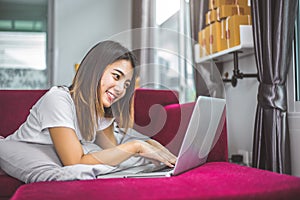 Young woman surfing the internet by laptop on red sofa in cheerful gesture mood emotion. Selling and online shopping concept.