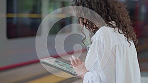 young woman is surfing internet by tablet waiting train on platform, shopping online, browsing site