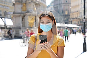 Young woman with surgical mask and mobile phone on the street of Vienna, Austria