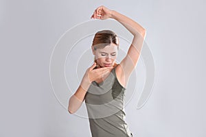 Young woman with sweat stain on her clothes against light background