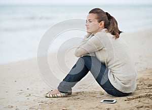 Young woman in sweater with cell phone sitting on lonely beach