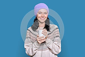 Young woman in sweater hat with mug on blue background