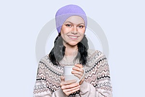 Young woman in sweater hat with mug on light studio background