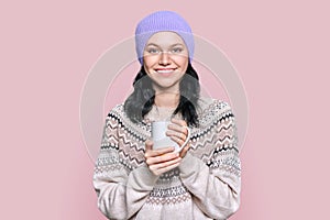 Young woman in sweater hat with mug on pink background