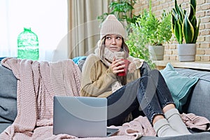 Young woman in sweater hat sitting at home, basking with cup of hot drink