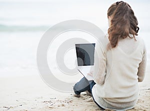 Young woman in sweater sitting on lonely beach and