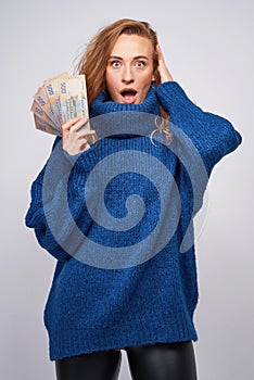 young woman in a sweater is surprised by money, on a gray background.