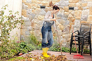 Young woman sweeping autumn leaves veranda
