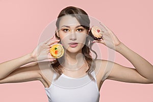 Young woman with a sweet donut in her hands. Portrait on a pink background