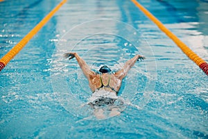 Young woman swimmer swims in swimming pool. Back view.