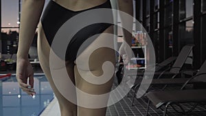 Young woman swimmer walking on background swimming pool in health club