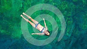 Young woman swimming in blue sea lagoon in crystal clear water, girl in bikini swims and relax, aerial view from above