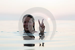 Young woman swimming in the sea showing a peace sign